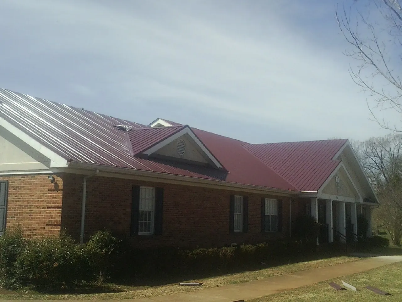 Red metal roof with gabled entries on a long brick building, from a Hail Damage Roof Repair job in Jericho