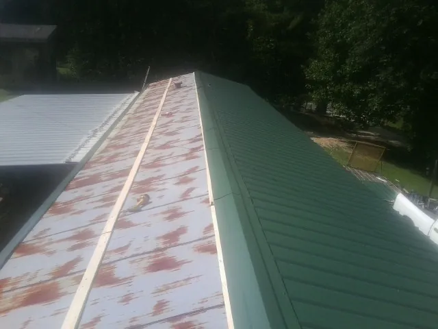 Old rusted panels beside newly installed green metal roofing — Wind Damage Roof Repair by Roofing Brothers in Jericho