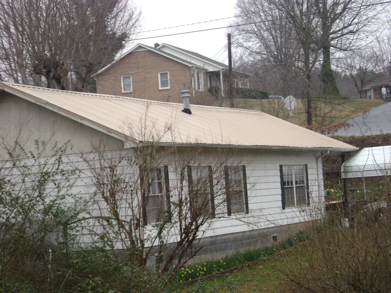 Tan metal roof on a white sided house set into a hillside — Commercial Roofing by Roofing Brothers in Jericho